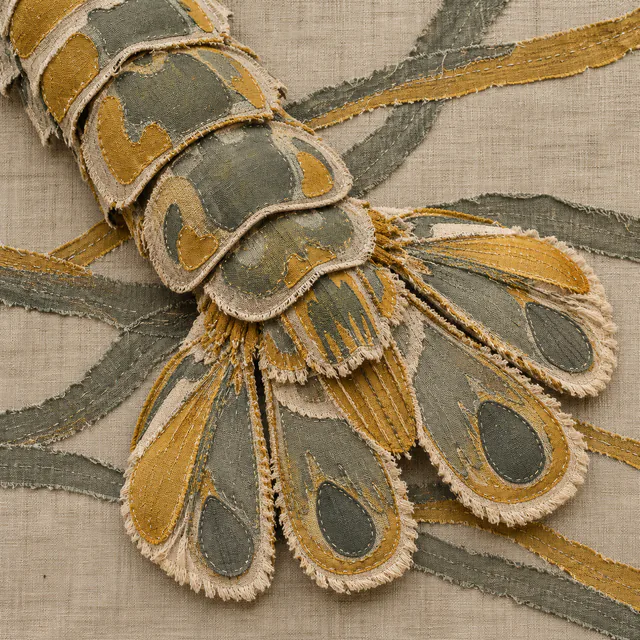Sage and mustard cloth patches form a cropped segmented tail and broad fan over crossing strips on natural linen.